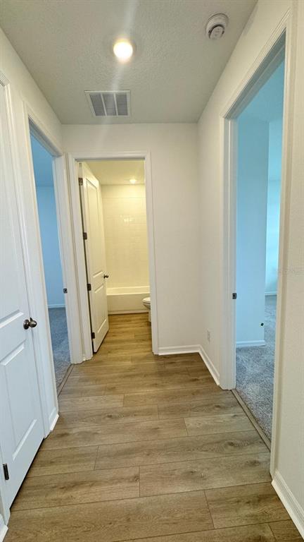 A hallway with wood-look flooring leads to a bathroom with a white tub and toilet — 5746 CATTLE RANCH DR, ST CLOUD, FL