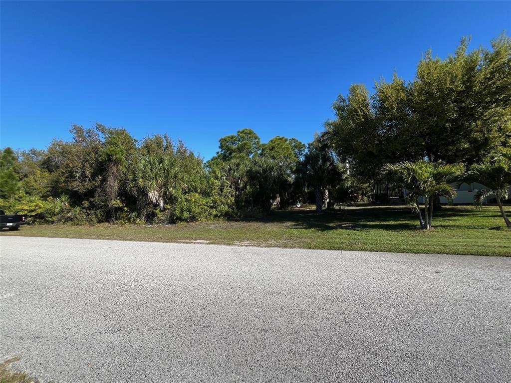 A vacant, grassy lot with trees and shrubs sits beside a paved road — 8410 TOPEKA CIRCLE, PORT CHARLOTTE, FL