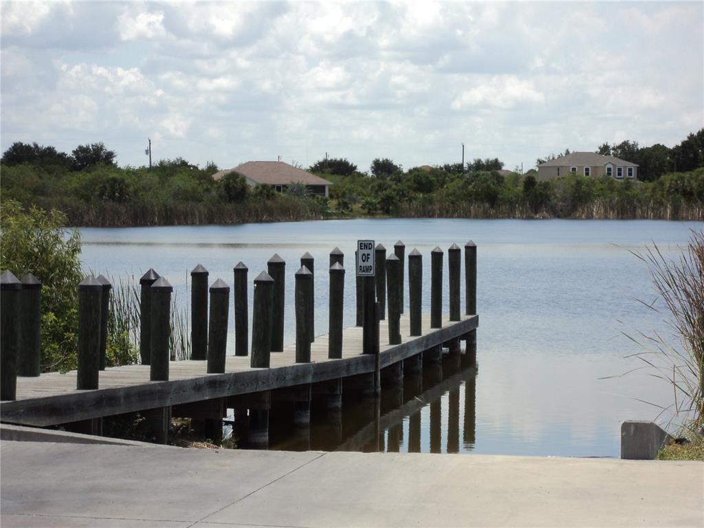 A wooden boat dock extends into a lake from a concrete boat ramp — 8410 TOPEKA CIRCLE, PORT CHARLOTTE, FL