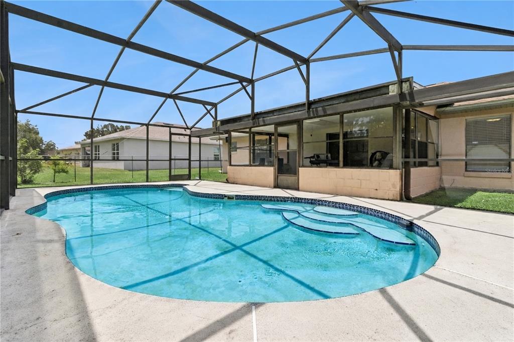 A swimming pool with built-in steps sits inside a screened-in patio enclosure — 909 SAN MARCO DR, KISSIMMEE, FL