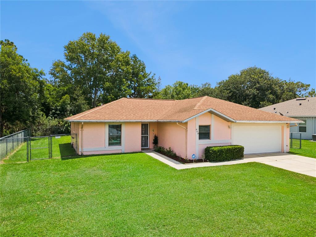 A single-story pink house with a brown roof, a two-car garage, and a front lawn — 909 SAN MARCO DR, KISSIMMEE, FL