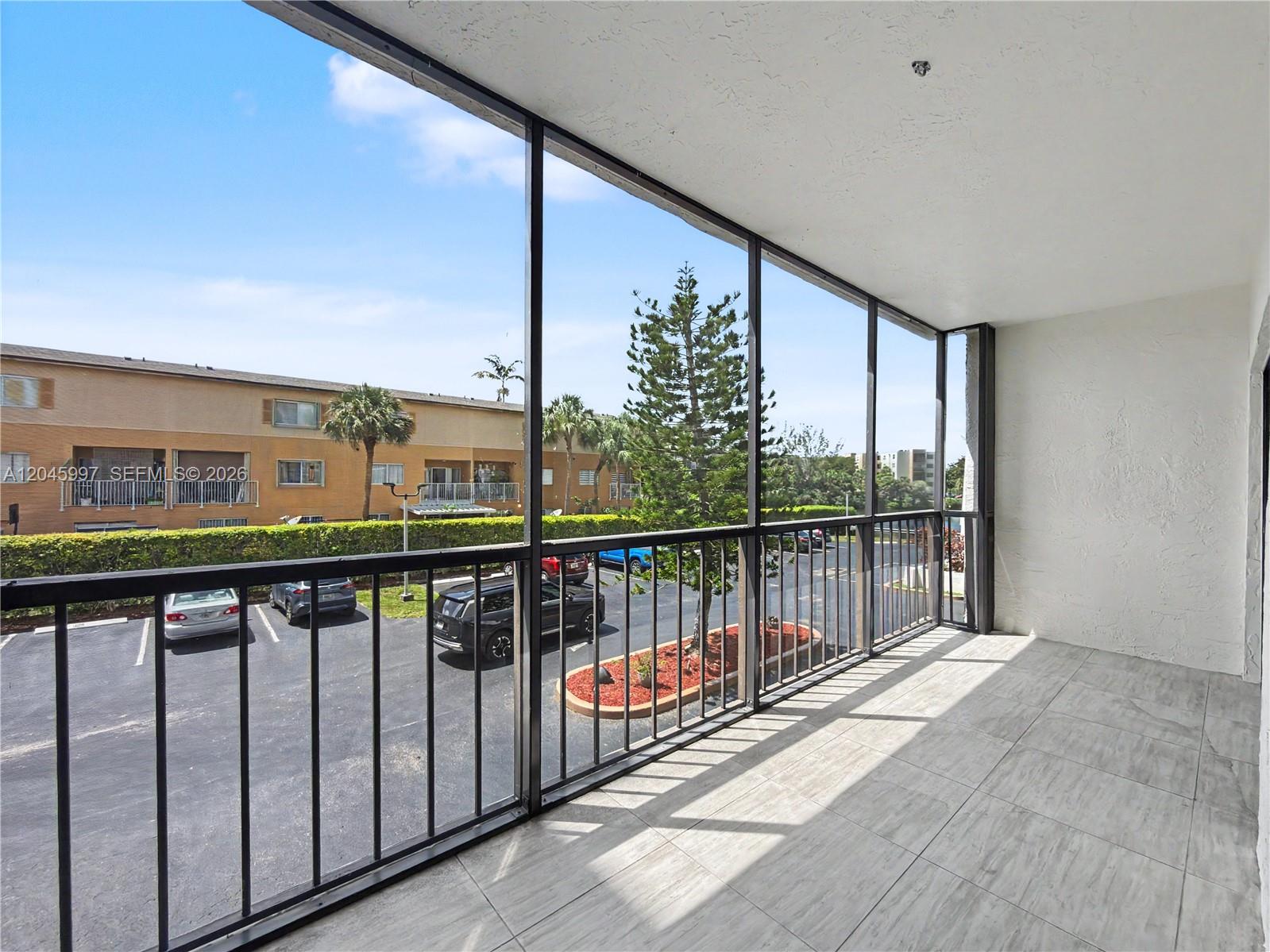 A screened-in balcony features light-colored tile flooring and overlooks a parking lot and trees — 14203 SW 66th St # 103, Miami FL 33183, MIAMI, FL