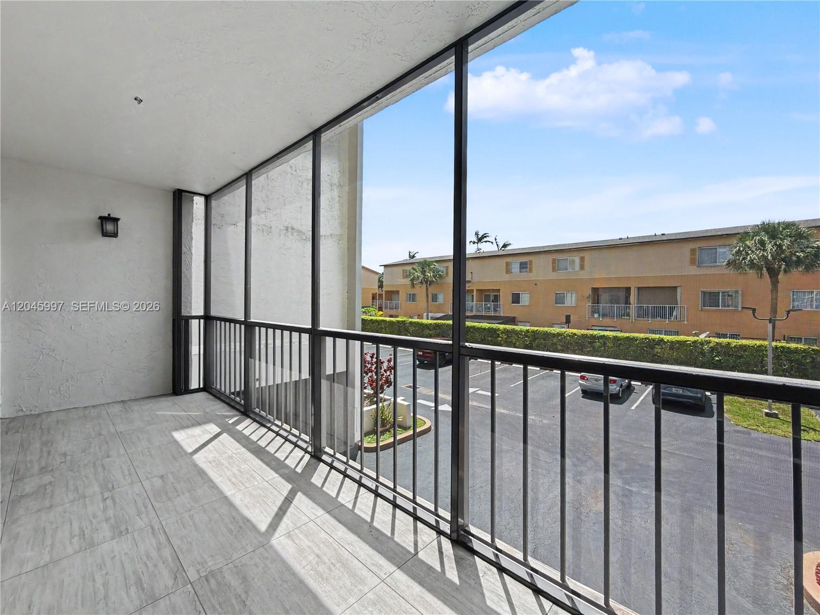 A screened-in balcony features light-colored tile flooring and a view of a parking lot — 14203 SW 66th St # 103, Miami FL 33183, MIAMI, FL