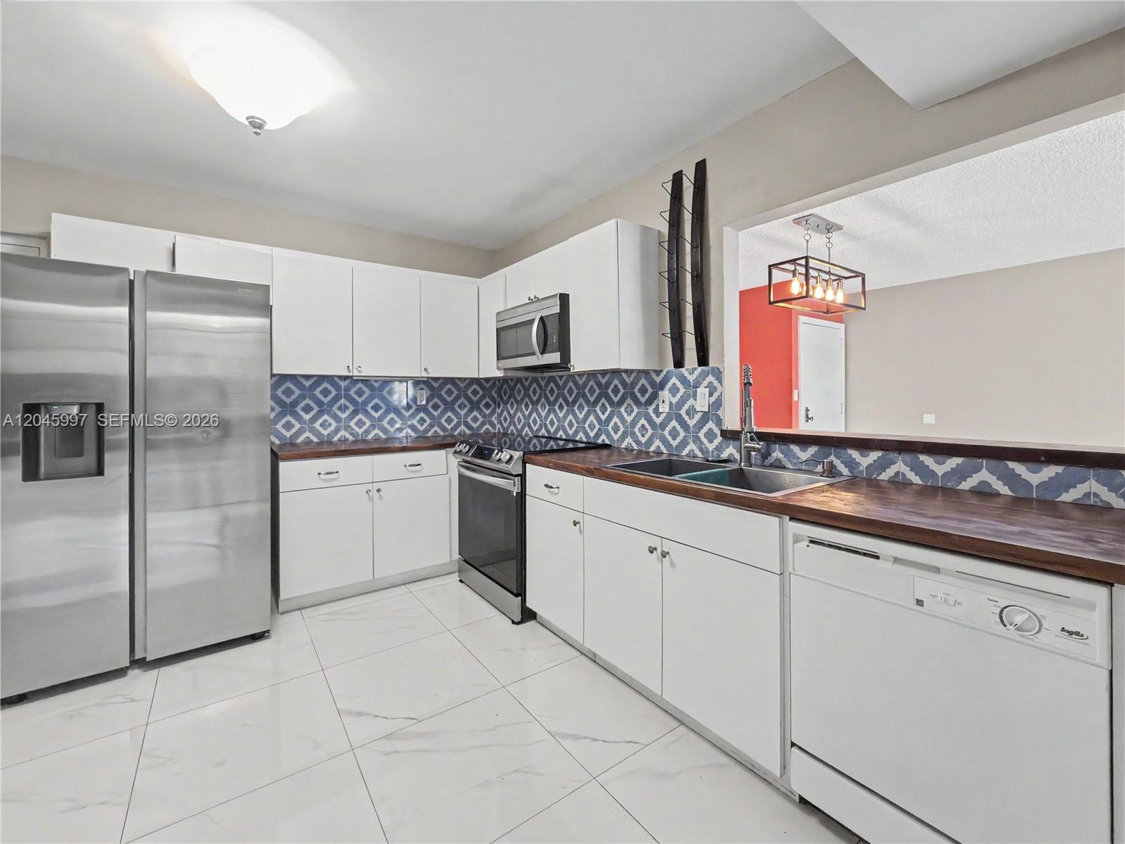 A kitchen features white cabinets, stainless steel appliances, a wood countertop, and patterned blue backsplash — 14203 SW 66th St # 103, Miami FL 33183, MIAMI, FL