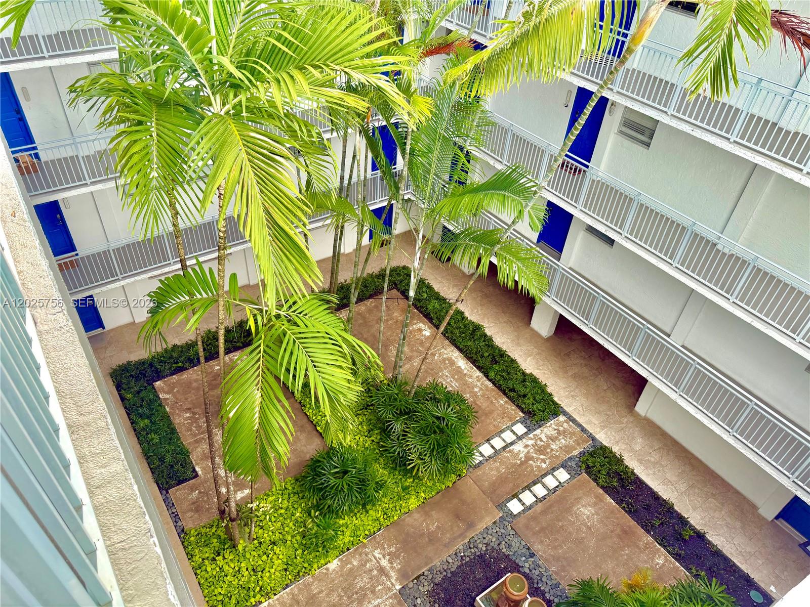 An elevated view of a courtyard with palm trees, walkways, and multi-story apartment balconies — 777 NE 62nd St # C512, Miami FL 33138, MIAMI, FL