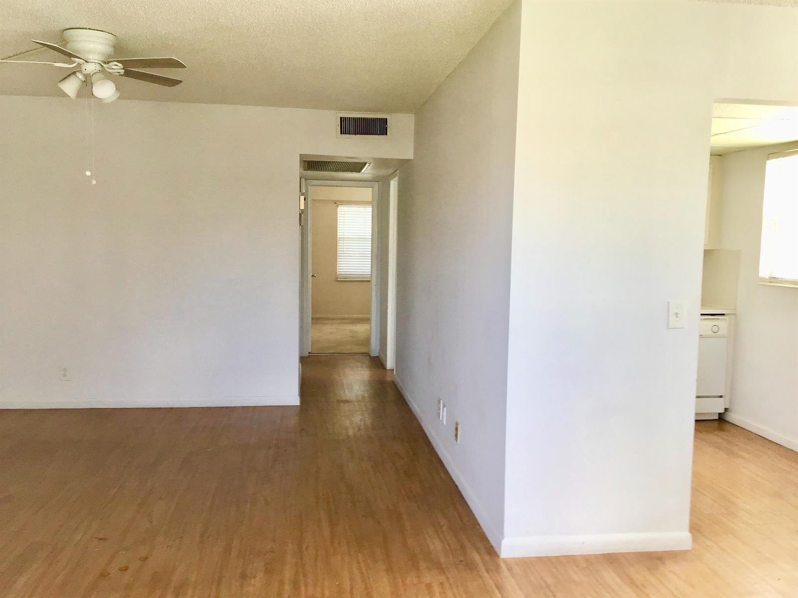 An interior view shows a living area with wood-look flooring, a ceiling fan, and hallway — 84 Brighton B, Boca Raton FL 33434, BOCA RATON, FL