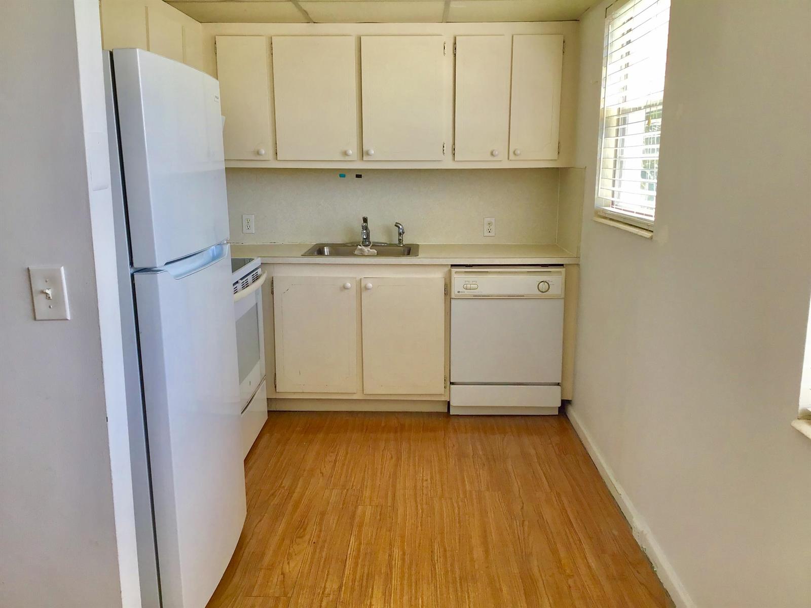 A small kitchen features white appliances, light-colored cabinets, a sink, and wood-look flooring — 84 Brighton B, Boca Raton FL 33434, BOCA RATON, FL