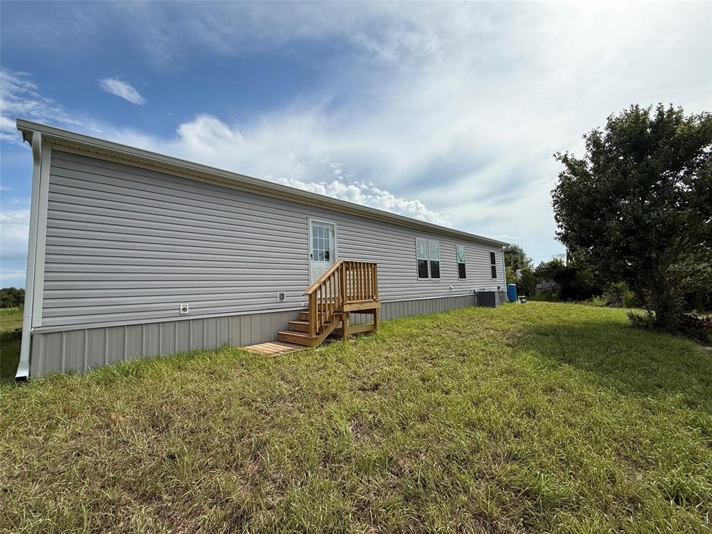 A long, light gray manufactured home exterior features a wooden staircase leading to a side door — 20263 NW 304TH STREET, OKEECHOBEE, FL