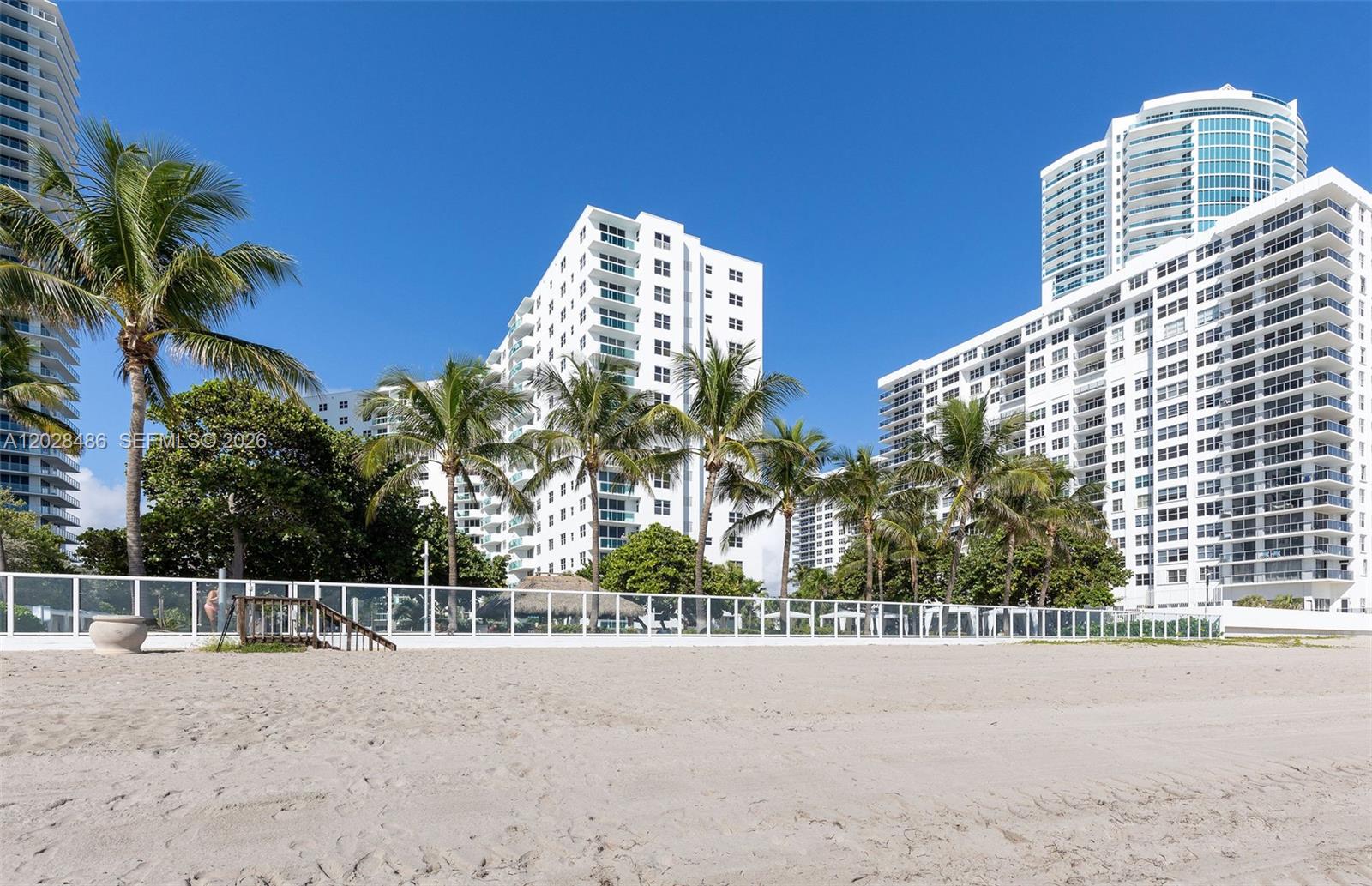 A sandy beach leads to a white fence in front of several tall residential buildings — 3001 S Ocean Dr # 227, Hollywood FL 33019, HOLLYWOOD, FL