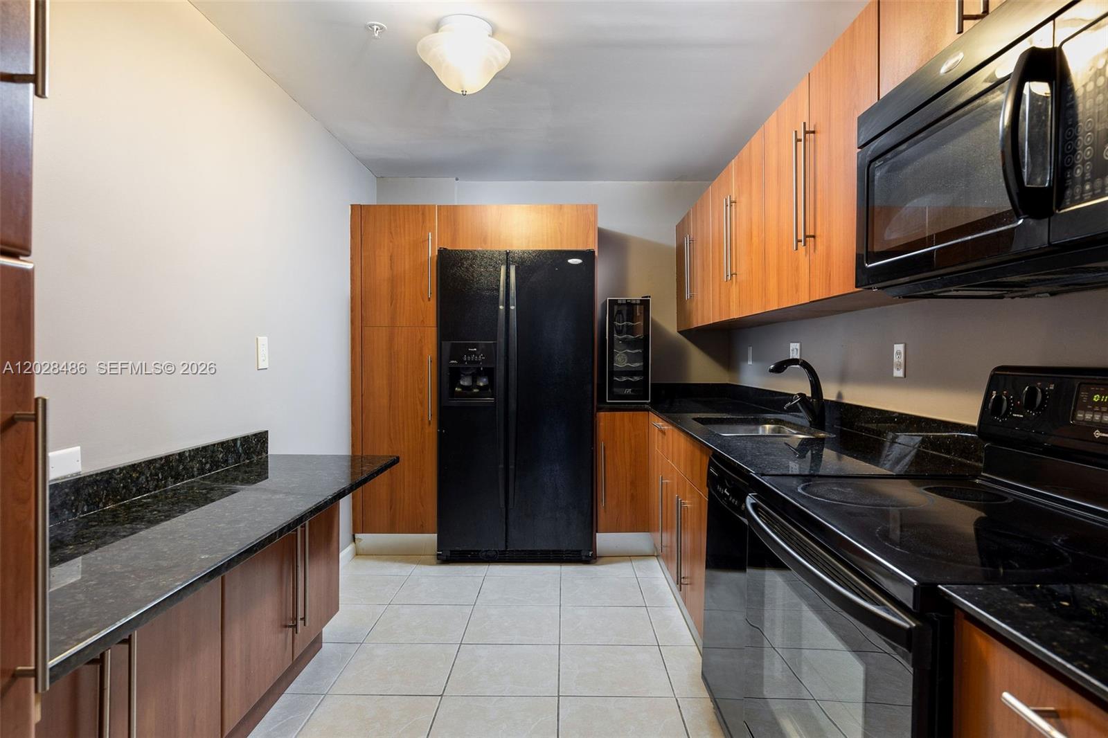 A kitchen features wood cabinets, black appliances, and dark granite countertops on a tiled floor — 3001 S Ocean Dr # 227, Hollywood FL 33019, HOLLYWOOD, FL