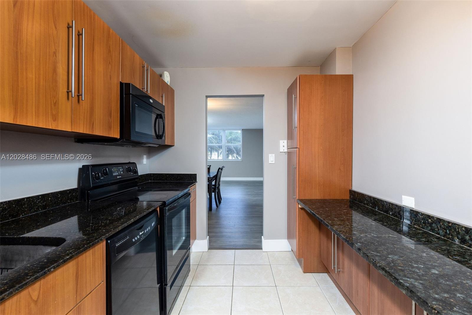 A kitchen features wood cabinets, black appliances, and dark granite countertops on a tiled floor — 3001 S Ocean Dr # 227, Hollywood FL 33019, HOLLYWOOD, FL