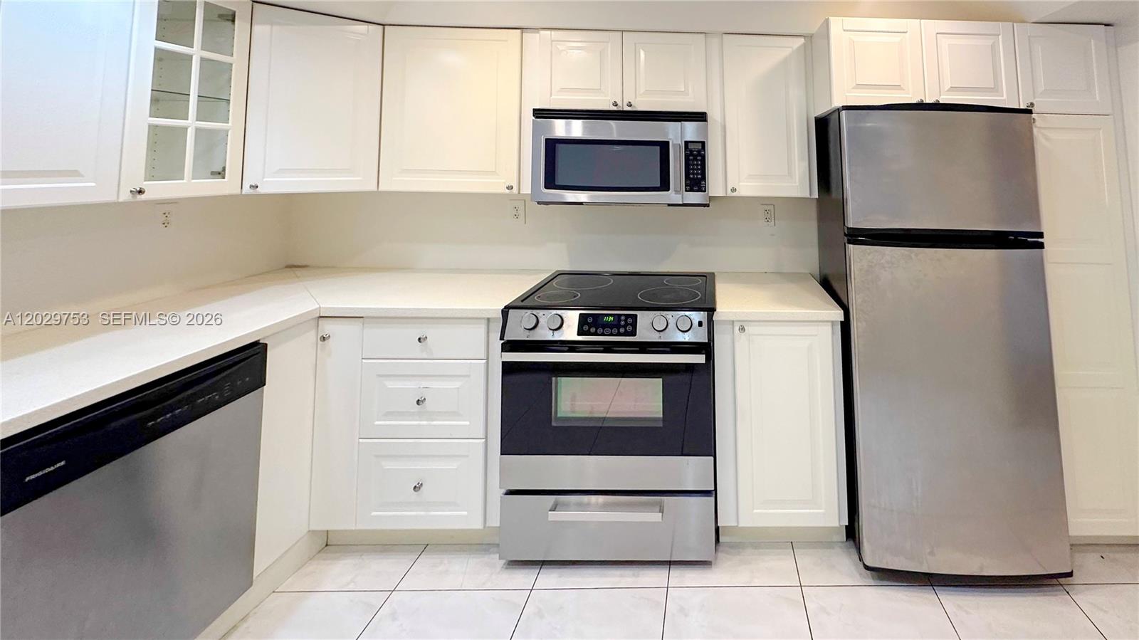 A kitchen features white cabinetry, stainless steel appliances, and light-colored countertops and floor tiles — 800 Parkview Dr # 323, Hallandale Beach FL 33009, HALLANDALE BEACH, FL