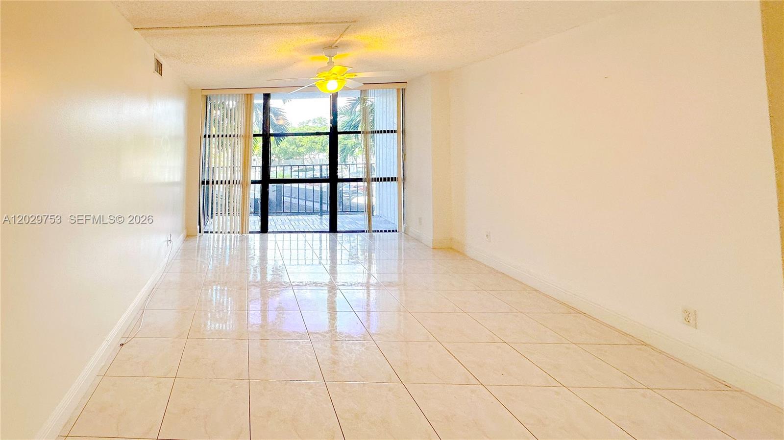 An empty living room features light-colored tile flooring, white walls, and a sliding glass door — 800 Parkview Dr # 323, Hallandale Beach FL 33009, HALLANDALE BEACH, FL