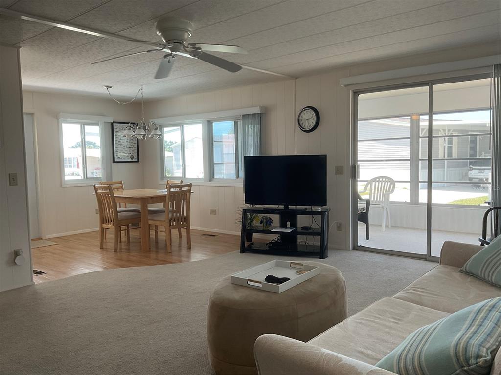 A living room and dining area with carpet, wood flooring, a ceiling fan, and sliding doors — 213 COMO DRIVE, VENICE, FL