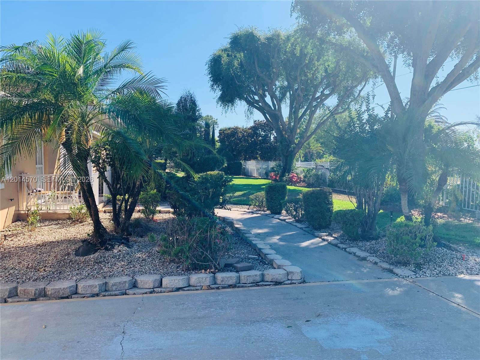 A paved walkway leads through a landscaped front yard with palm trees and mature trees — 196 JAMISON AVE, Lake Placid FL 33852, LAKE PLACID, FL