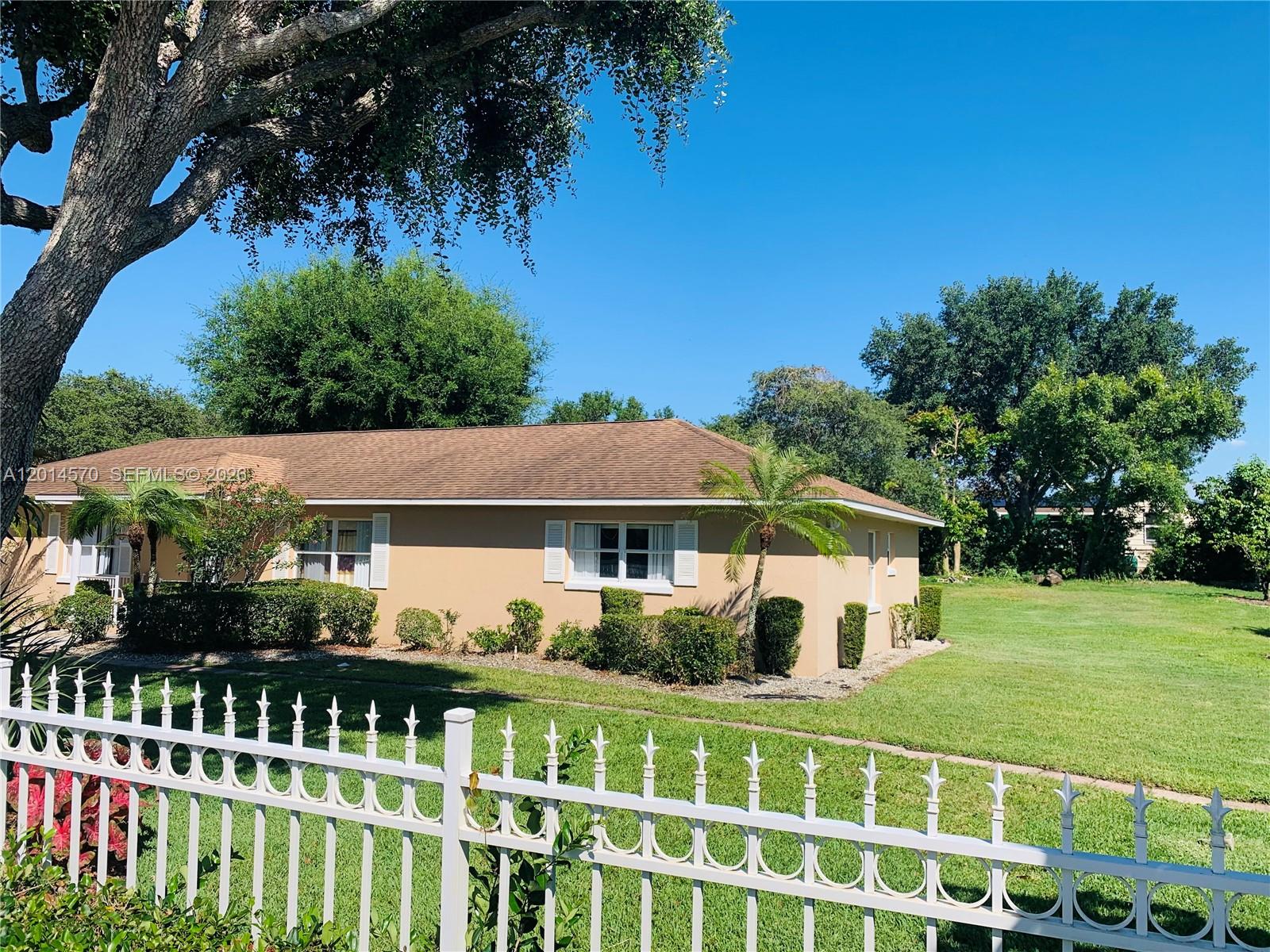 A single-story tan house with a brown roof sits behind a white metal fence — 196 JAMISON AVE, Lake Placid FL 33852, LAKE PLACID, FL