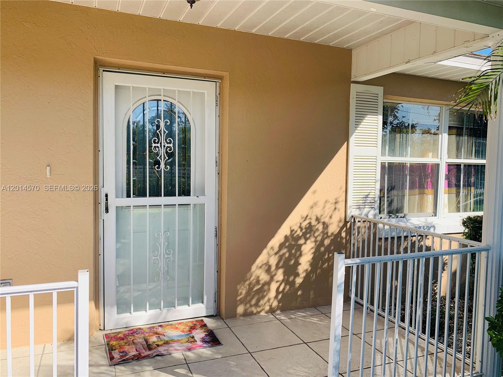 A tan exterior wall features a white storm door and a window with white shutters — 196 JAMISON AVE, Lake Placid FL 33852, LAKE PLACID, FL