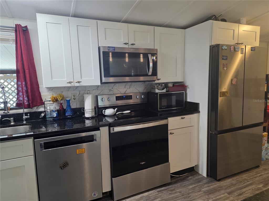 A kitchen features white cabinets, stainless steel appliances, and black countertops — 1855 BRAMBLEWOOD DRIVE, ST CLOUD, FL
