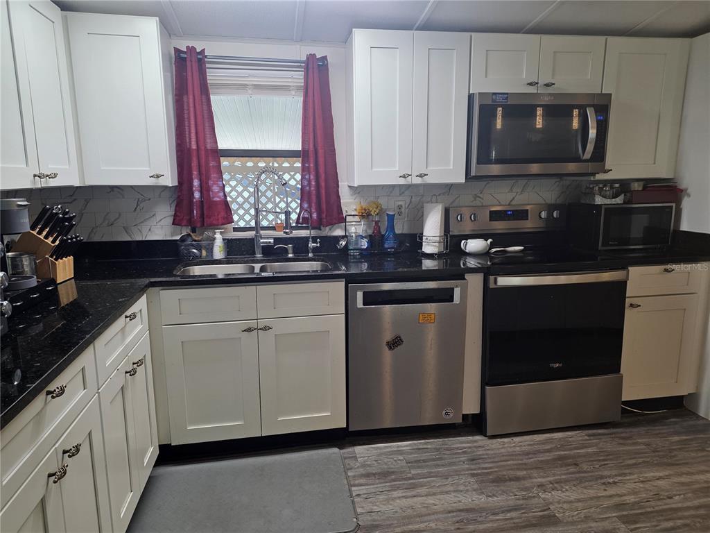 A kitchen features white cabinets, black countertops, stainless steel appliances, and a window with curtains — 1855 BRAMBLEWOOD DRIVE, ST CLOUD, FL