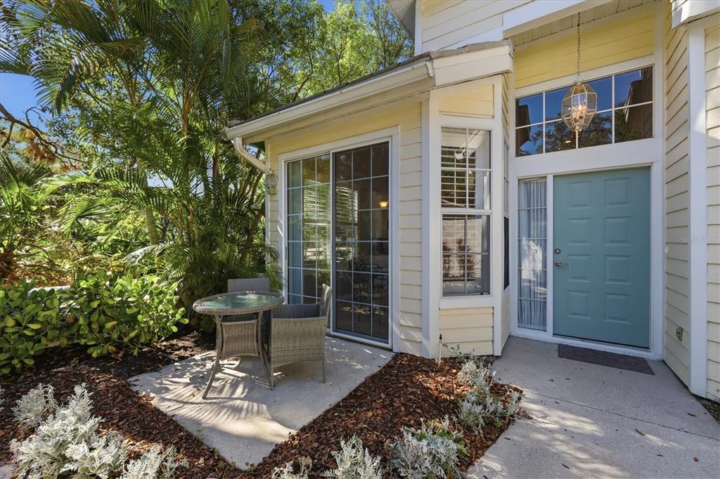 A patio with a small table and chairs sits beside a yellow house with a door — 7906 WHITEBRIDGE GLEN, UNIVERSITY PARK, FL