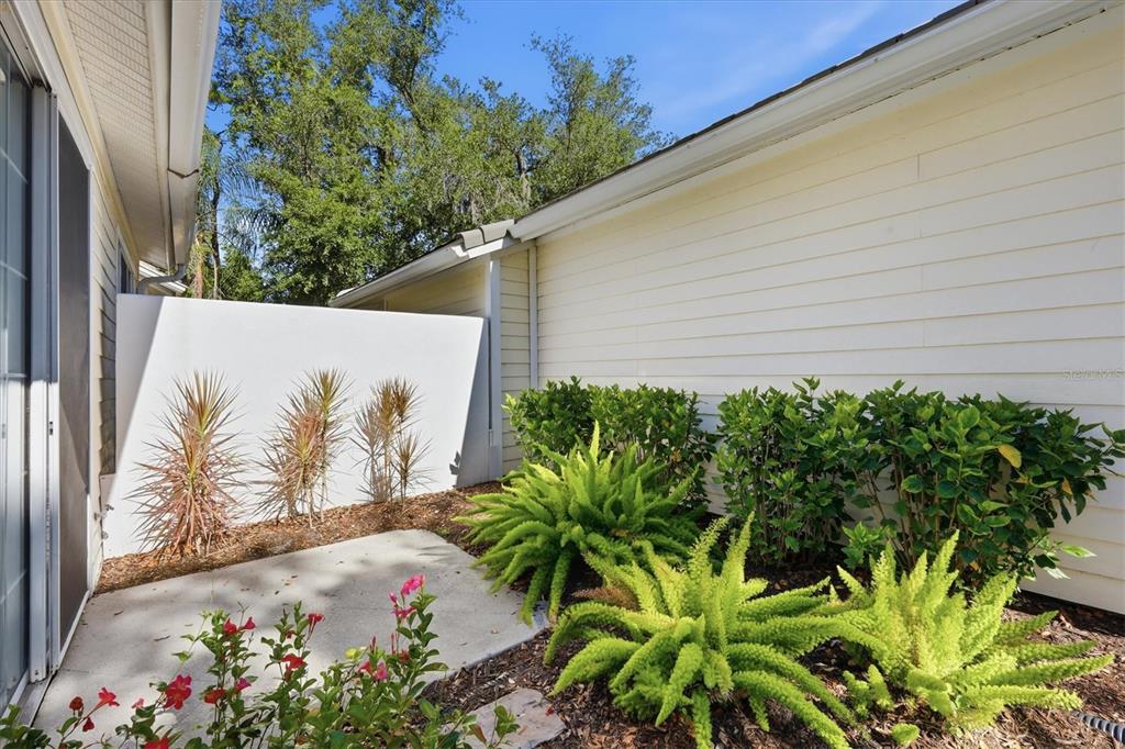A concrete patio sits beside a house with light-colored siding and a privacy wall — 7906 WHITEBRIDGE GLEN, UNIVERSITY PARK, FL