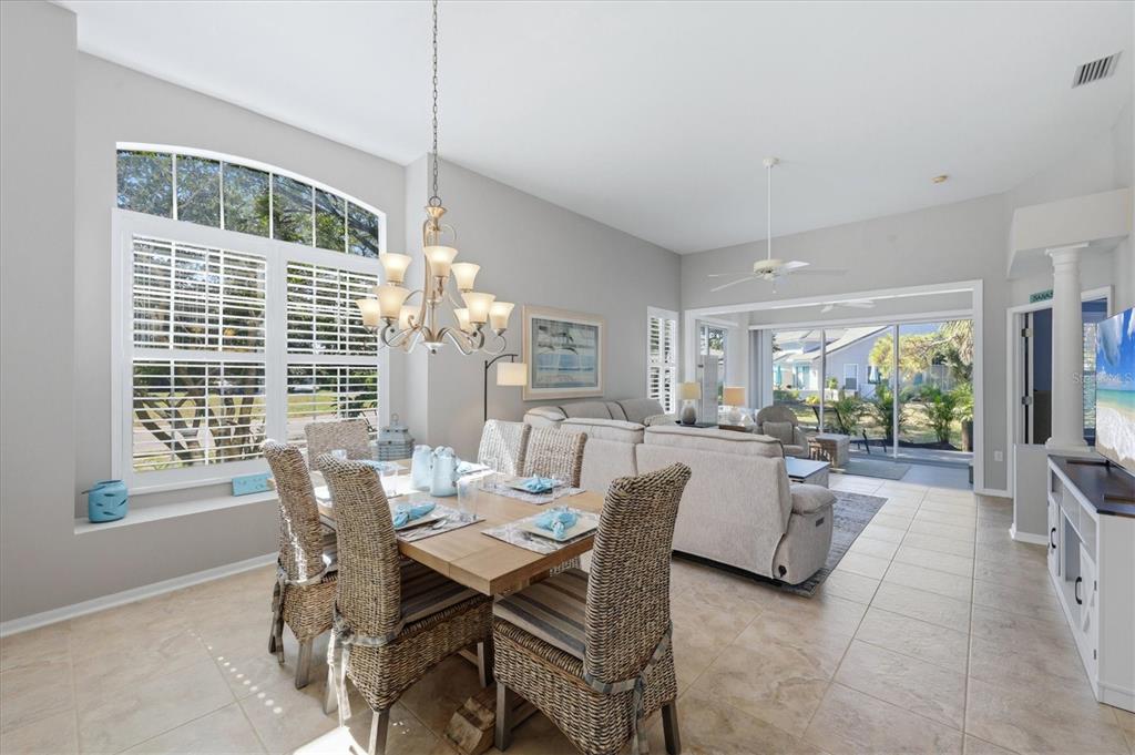 A dining area with wicker chairs and a chandelier opens into a living room — 7906 WHITEBRIDGE GLEN, UNIVERSITY PARK, FL