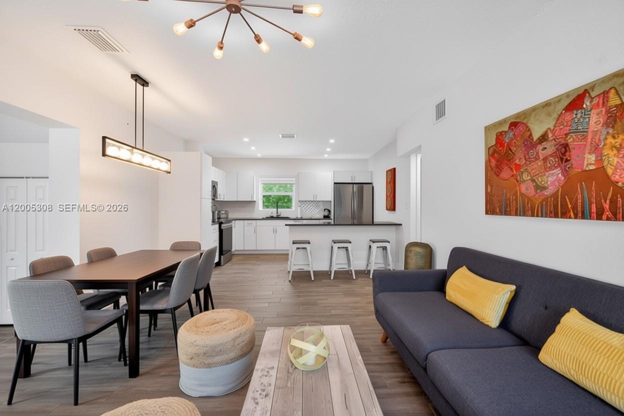 An open-concept living and dining area features a kitchen with white cabinets and wood-look flooring — 541 NW 109th St, Miami FL 33168, MIAMI, FL