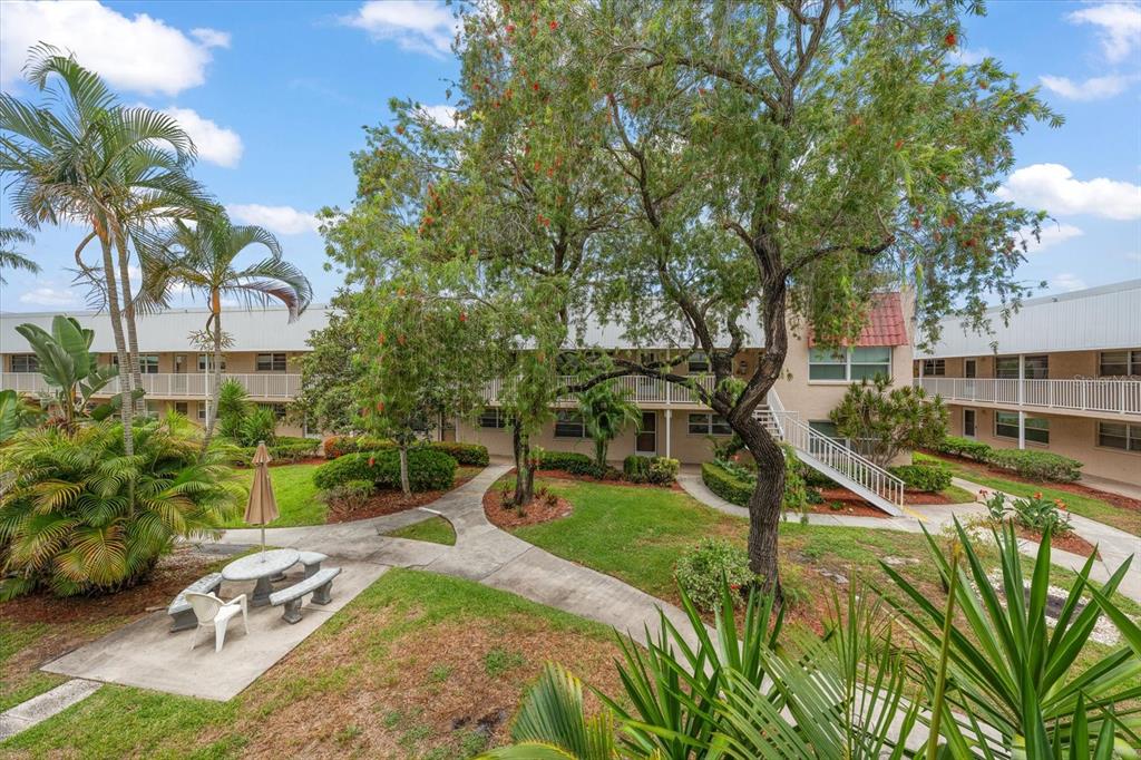 An exterior view of a multi-story apartment complex with a courtyard, trees, and walkways — 10033 64TH AVENUE N UNIT 19, ST PETERSBURG, FL