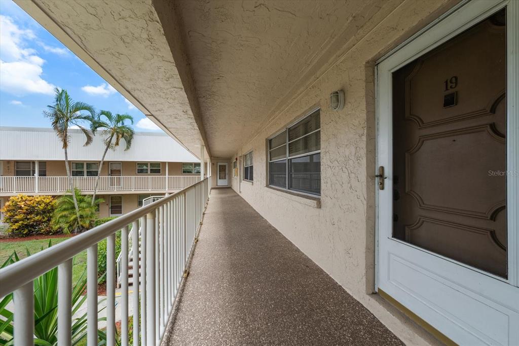 An exterior walkway leads past a door labeled 19 toward a multi-story apartment building — 10033 64TH AVENUE N UNIT 19, ST PETERSBURG, FL