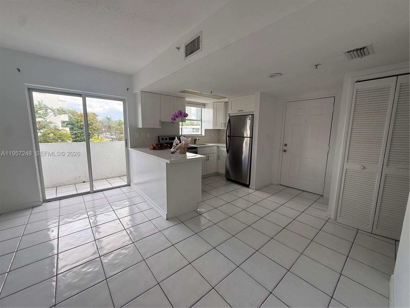 A kitchen with white cabinets and stainless steel appliances opens to a tiled living area — 3052 SW 27th Ave # 301, Miami FL 33133, MIAMI, FL