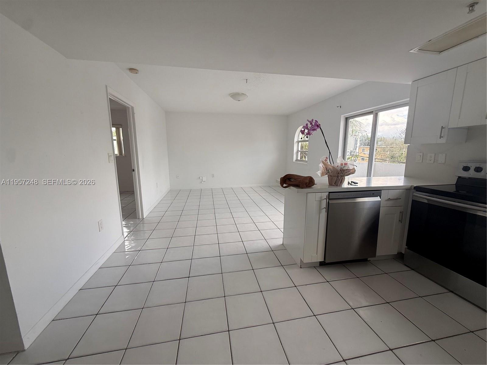 A kitchen with white cabinets and stainless steel appliances opens into a tiled living area — 3052 SW 27th Ave # 301, Miami FL 33133, MIAMI, FL