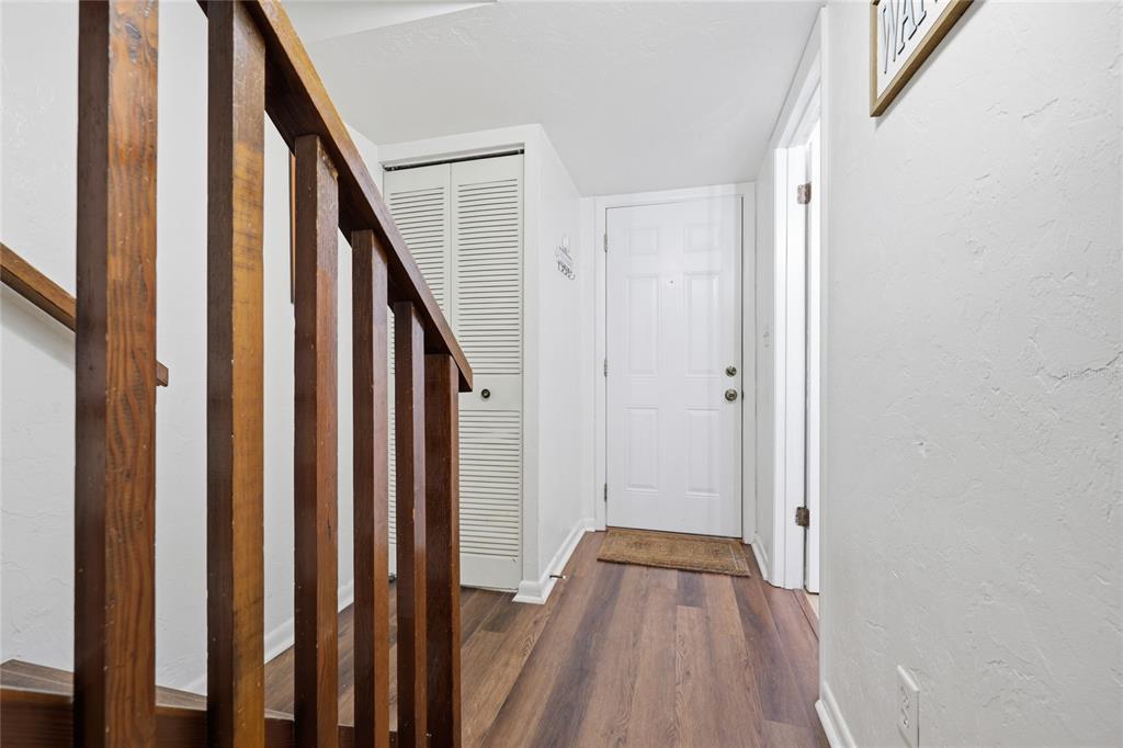A wooden staircase railing overlooks a hallway with wood-look flooring and a white front door — 3600 SW 19TH AVENUE UNIT 5D, GAINESVILLE, FL