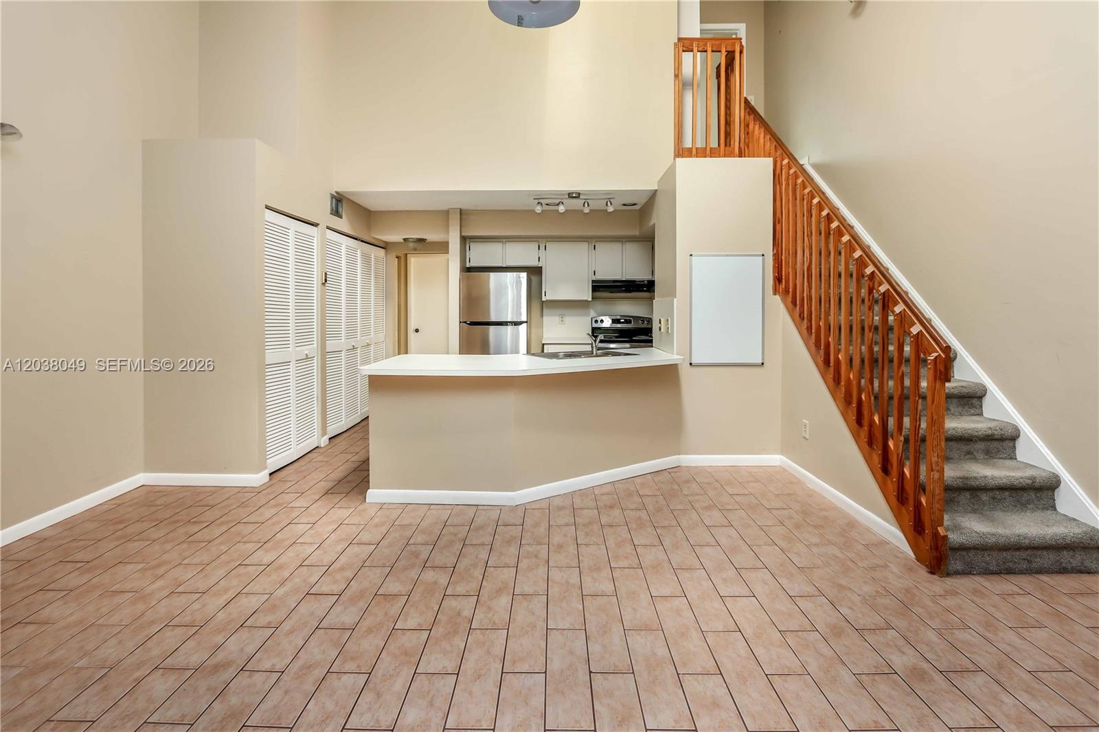 An open-plan kitchen with a breakfast bar sits beside a staircase in a tiled room — 444 SE 14th St, Dania Beach FL 33004, DANIA BEACH, FL