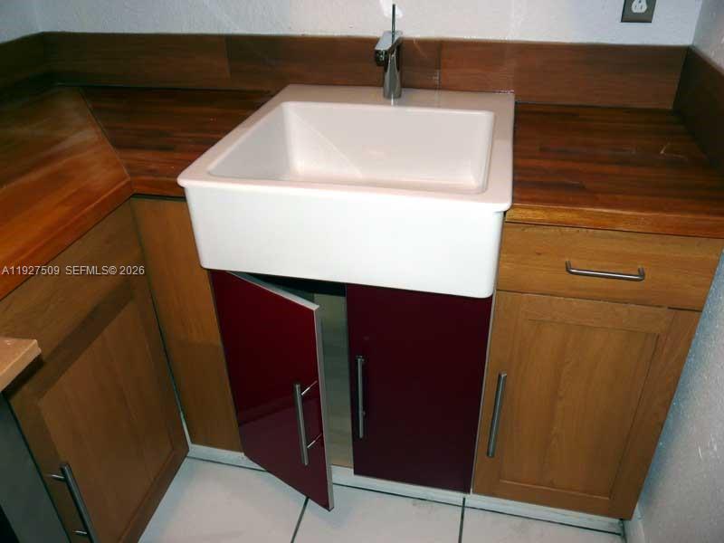 A white farmhouse sink is set into a wooden countertop with red and wood-toned cabinets — 1880 NW 68th Ter, Miami FL 33147, MIAMI, FL