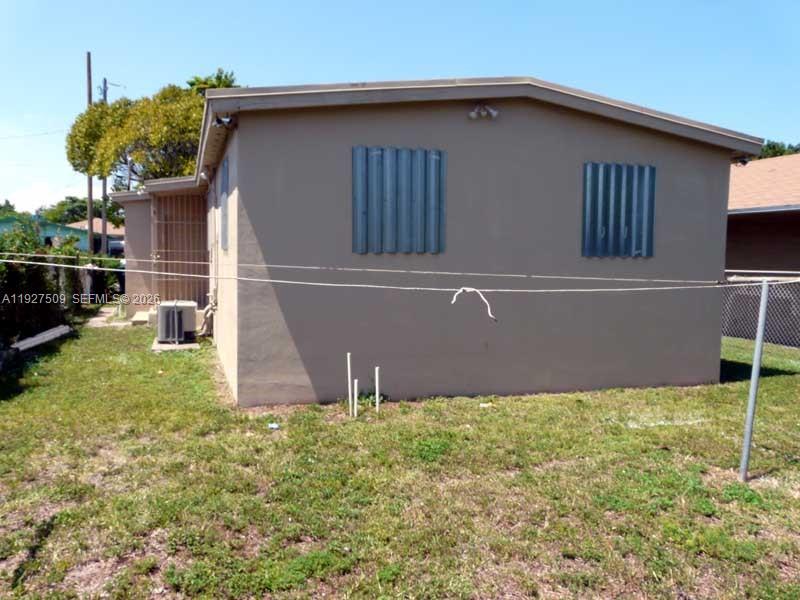 The exterior of a tan, single-story house features two windows with metal storm shutters — 1880 NW 68th Ter, Miami FL 33147, MIAMI, FL