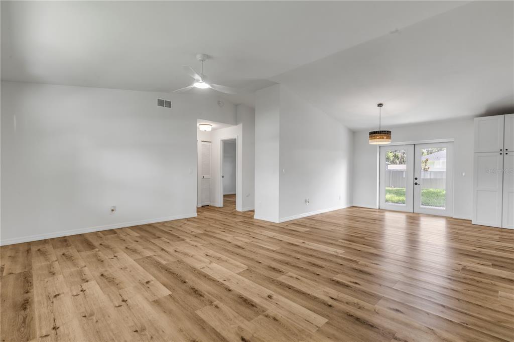 An open-concept living area features light wood-look flooring, white walls, a ceiling fan, and glass doors — 2119 LIME TREE DRIVE, EDGEWATER, FL