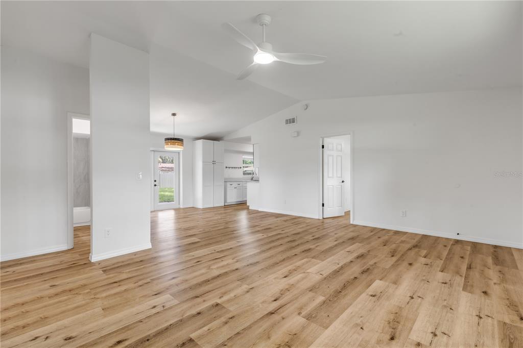 A bright, open-concept living area features light wood-look flooring, white walls, and a ceiling fan — 2119 LIME TREE DRIVE, EDGEWATER, FL