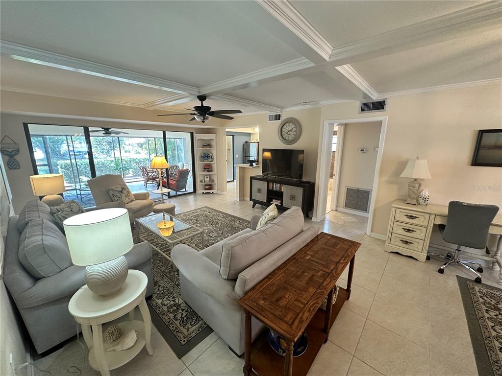 A living room with tile floors, a coffered ceiling, and a view of a screened patio — 4572 RED MAPLE ROAD UNIT 901, BRADENTON, FL