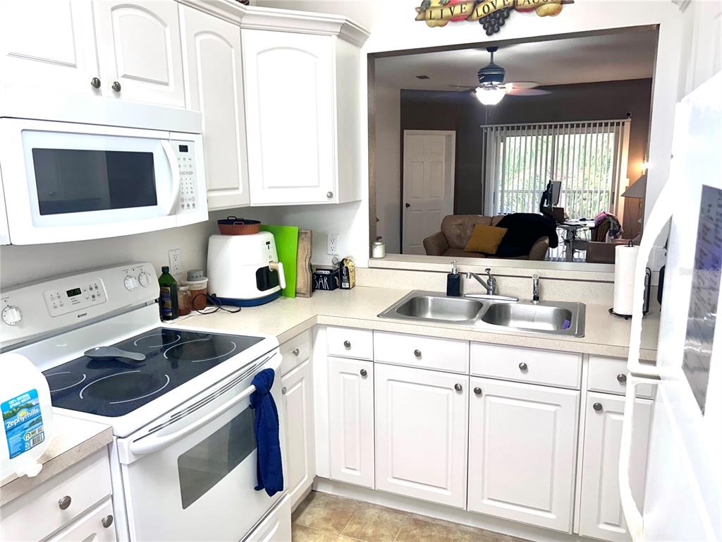 A kitchen features white cabinets, a white stove, a microwave, and beige laminate countertops — 8842 CORAL PALMS COURT UNIT B, KISSIMMEE, FL