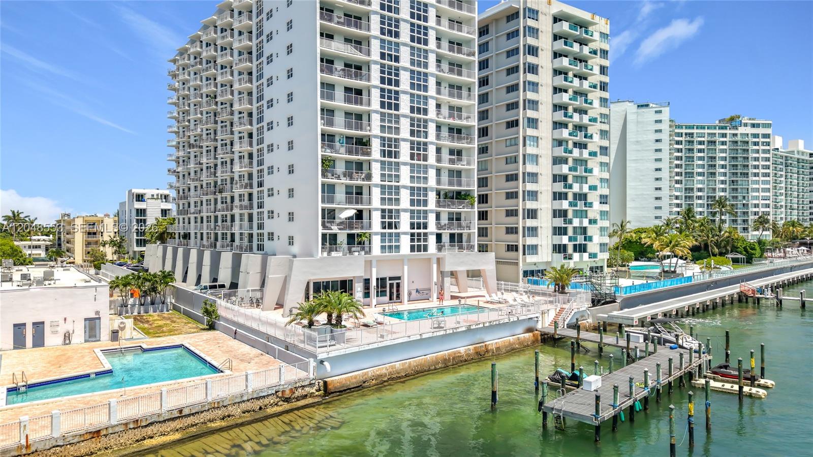An exterior view shows high-rise apartment buildings with swimming pools and a private boat dock — 1228 West Ave # 208, Miami Beach FL 33139, MIAMI BEACH, FL