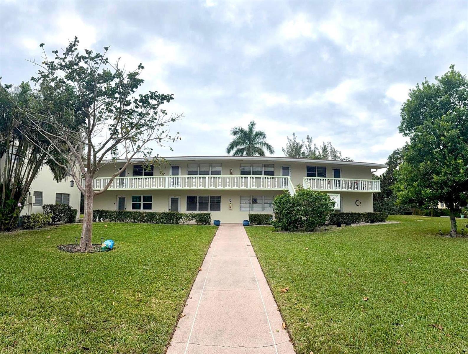 A two-story apartment building with a central walkway, white railings, and surrounding green lawn — 63 Windsor C, West Palm Beach FL 33417, WEST PALM BEACH, FL