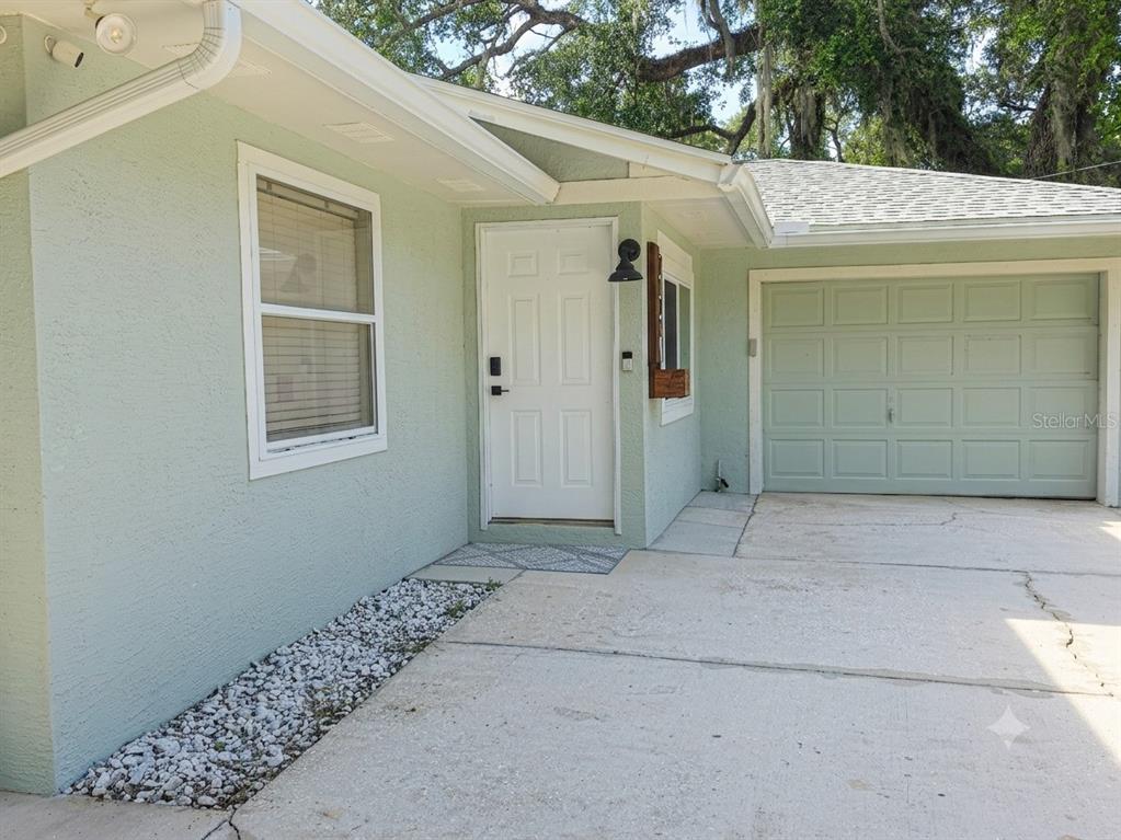 A light green house exterior features a white front door, a garage, and a gravel bed — 6806 S HOLLY OAK POINT, HOMOSASSA, FL