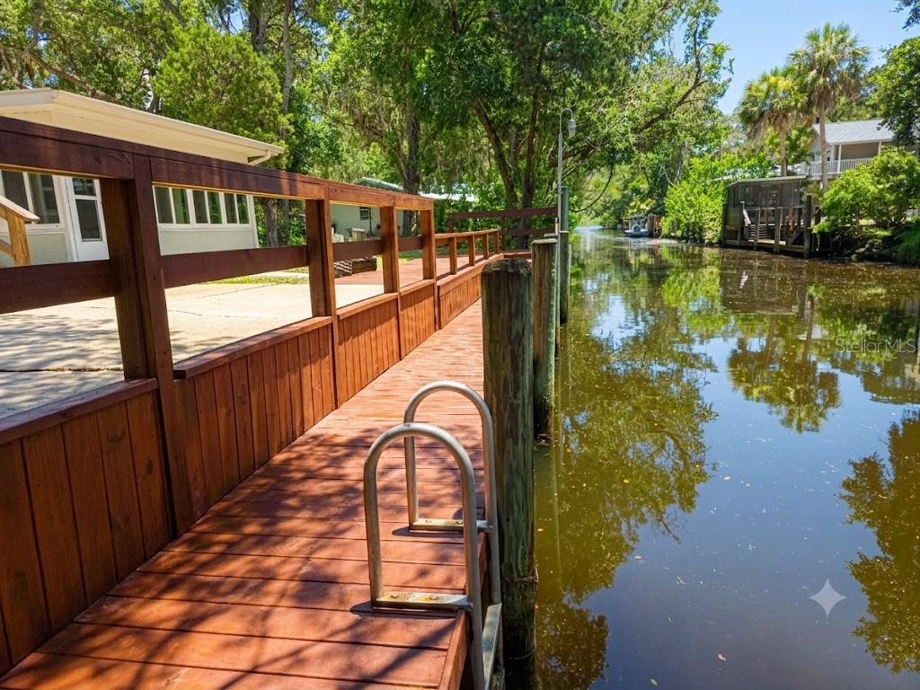 A wooden dock with a metal ladder extends along a narrow canal beside a house — 6806 S HOLLY OAK POINT, HOMOSASSA, FL