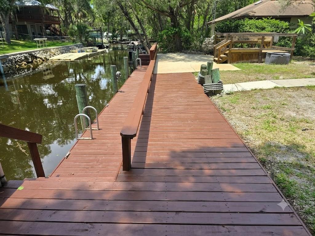 A wooden dock extends over a canal next to a grassy yard and wooden deck — 6806 S HOLLY OAK POINT, HOMOSASSA, FL