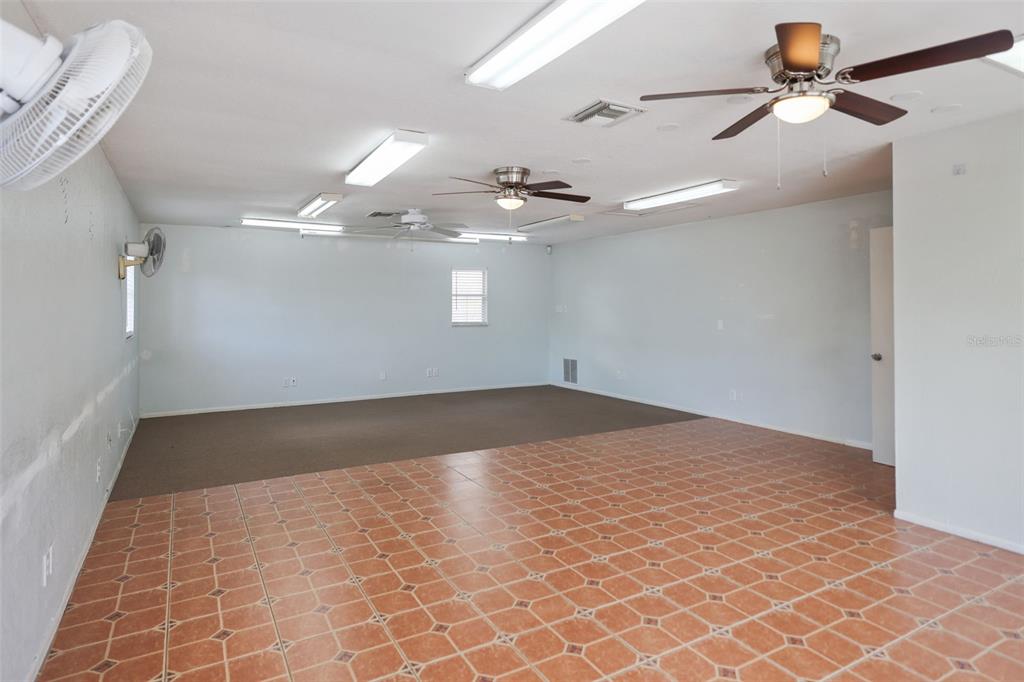 A large room features a tiled foreground, a carpeted area, ceiling fans, and fluorescent lighting — 167 6TH STREET SW, LARGO, FL