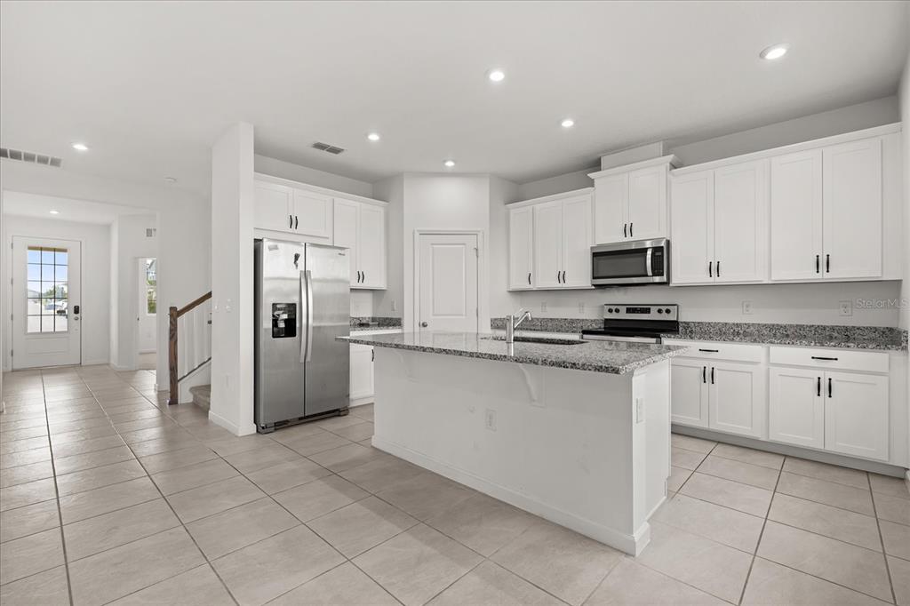 A kitchen features white cabinets, granite countertops, a center island, and stainless steel appliances — 1051 LAKESHORE BREEZE PLACE, KISSIMMEE, FL