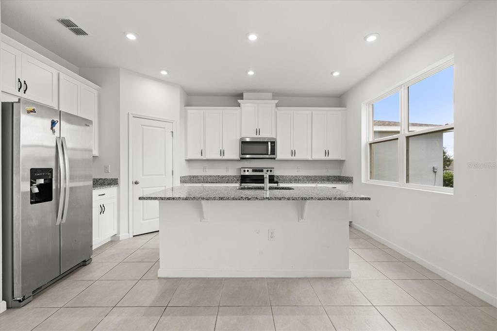 A kitchen features white cabinetry, granite countertops, a central island, and stainless steel appliances — 1051 LAKESHORE BREEZE PLACE, KISSIMMEE, FL