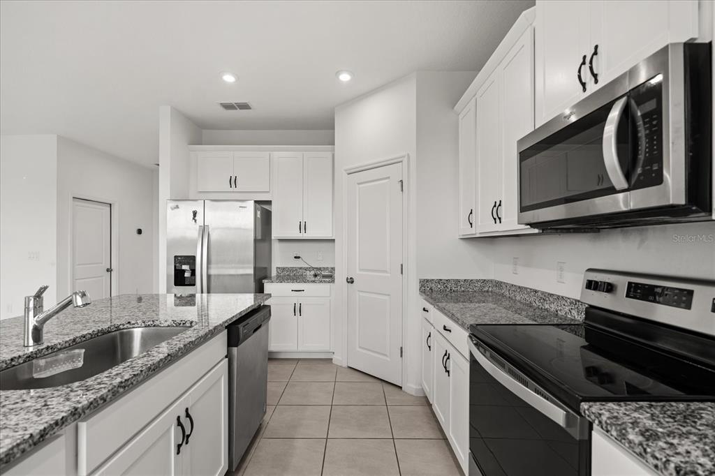 A kitchen with white cabinets, granite countertops, stainless steel appliances, and tile flooring — 1051 LAKESHORE BREEZE PLACE, KISSIMMEE, FL