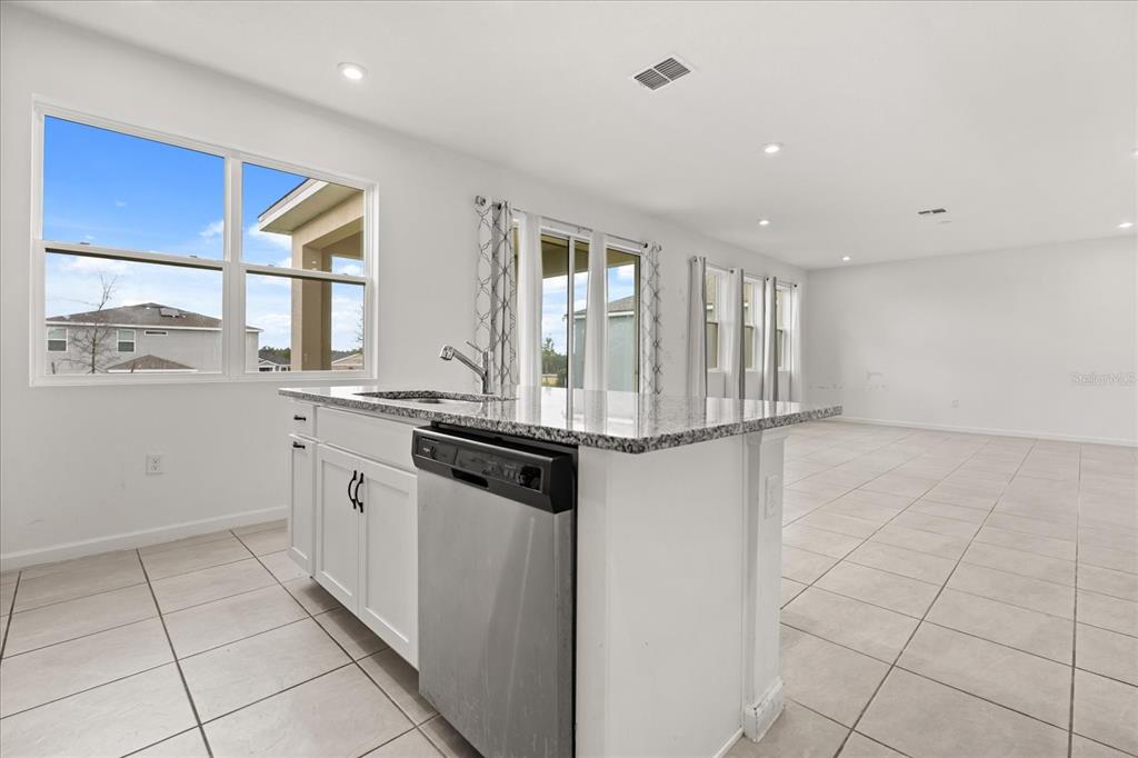 A kitchen island with a stainless steel dishwasher and granite countertop in an open-concept room — 1051 LAKESHORE BREEZE PLACE, KISSIMMEE, FL