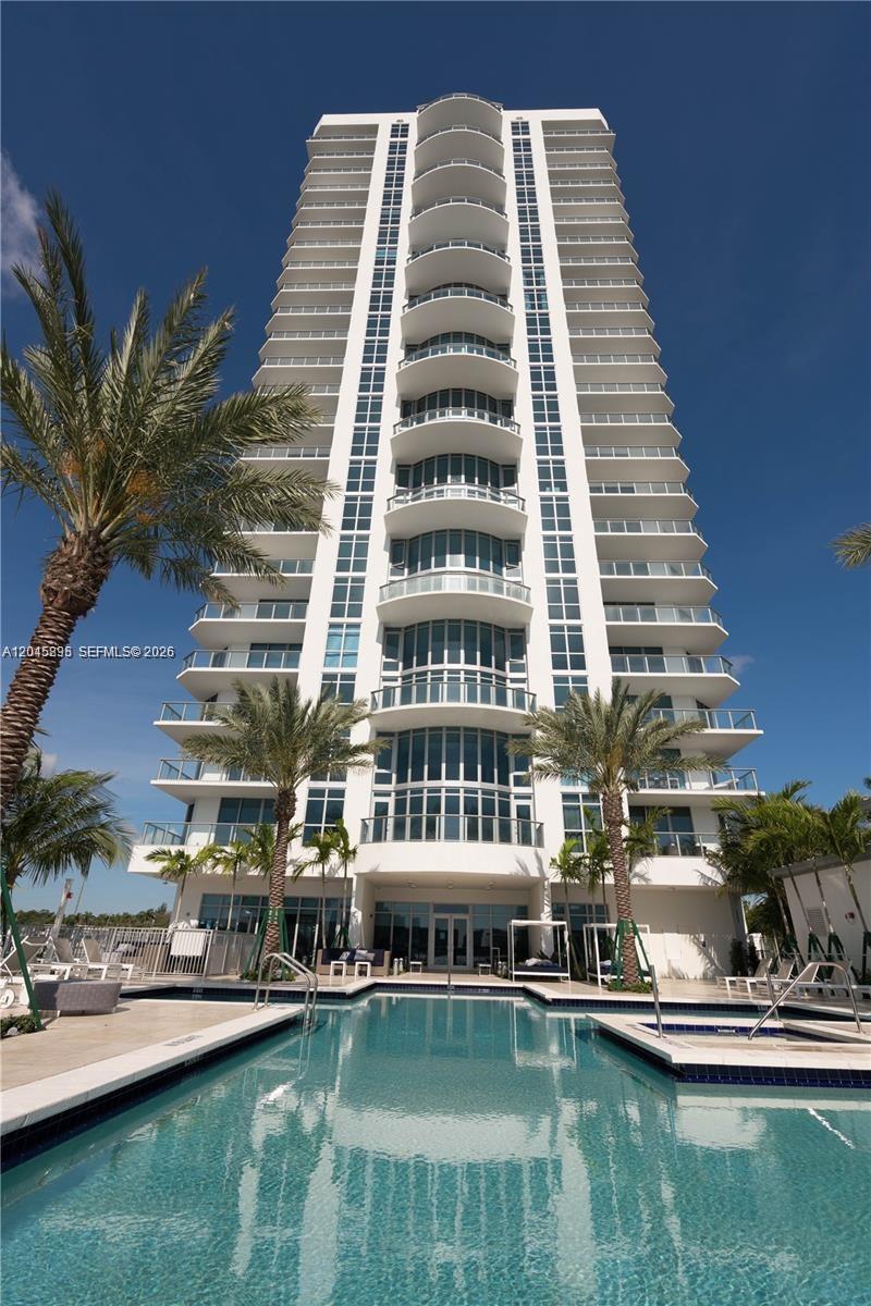 A tall white residential high-rise building stands behind a swimming pool and palm trees — NORTH MIAMI BEACH, FL